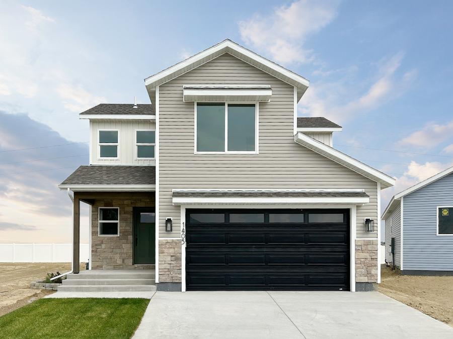 Exterior photo of charming 2-story home with 2-car garage, front porch, tan and white siding and brick accents